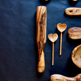 Olive wood muddler with two wooden heart spoons on a black surface