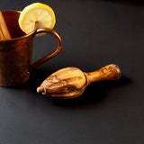 Olive Wood Citrus Reamer on black background with copper mug